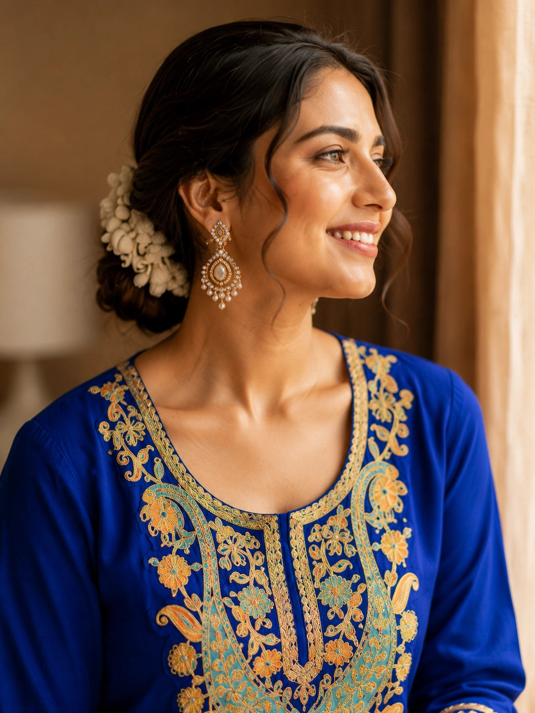 Woman in royal blue embroidered kurta with red pants, sitting by window.