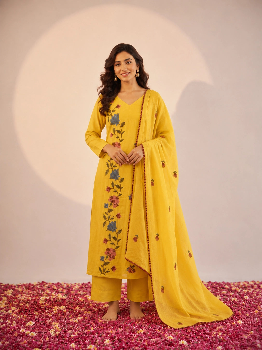 Woman in a vibrant yellow kurti set with colorful floral embroidery and dupatta.