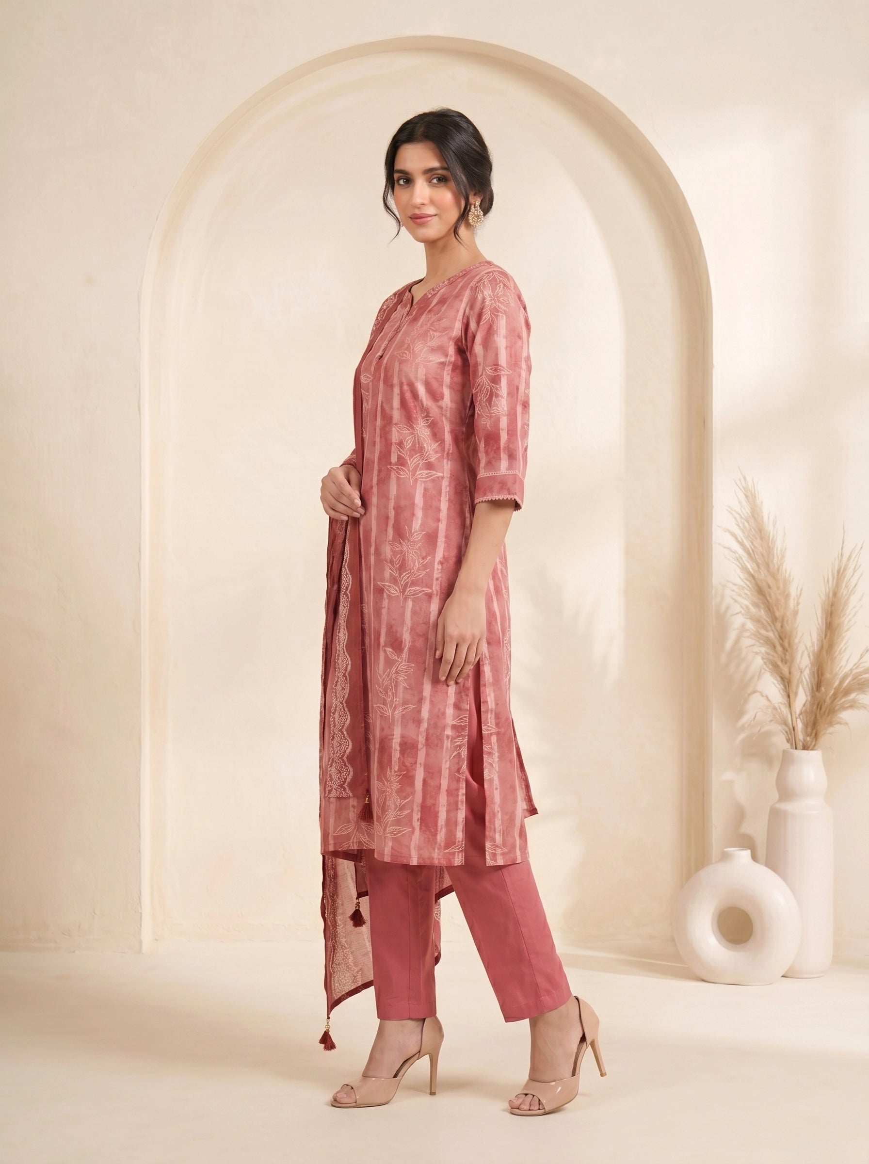 Woman wearing a rose pink printed kurti set with a dupatta, featuring leaf motifs and striped patterns.