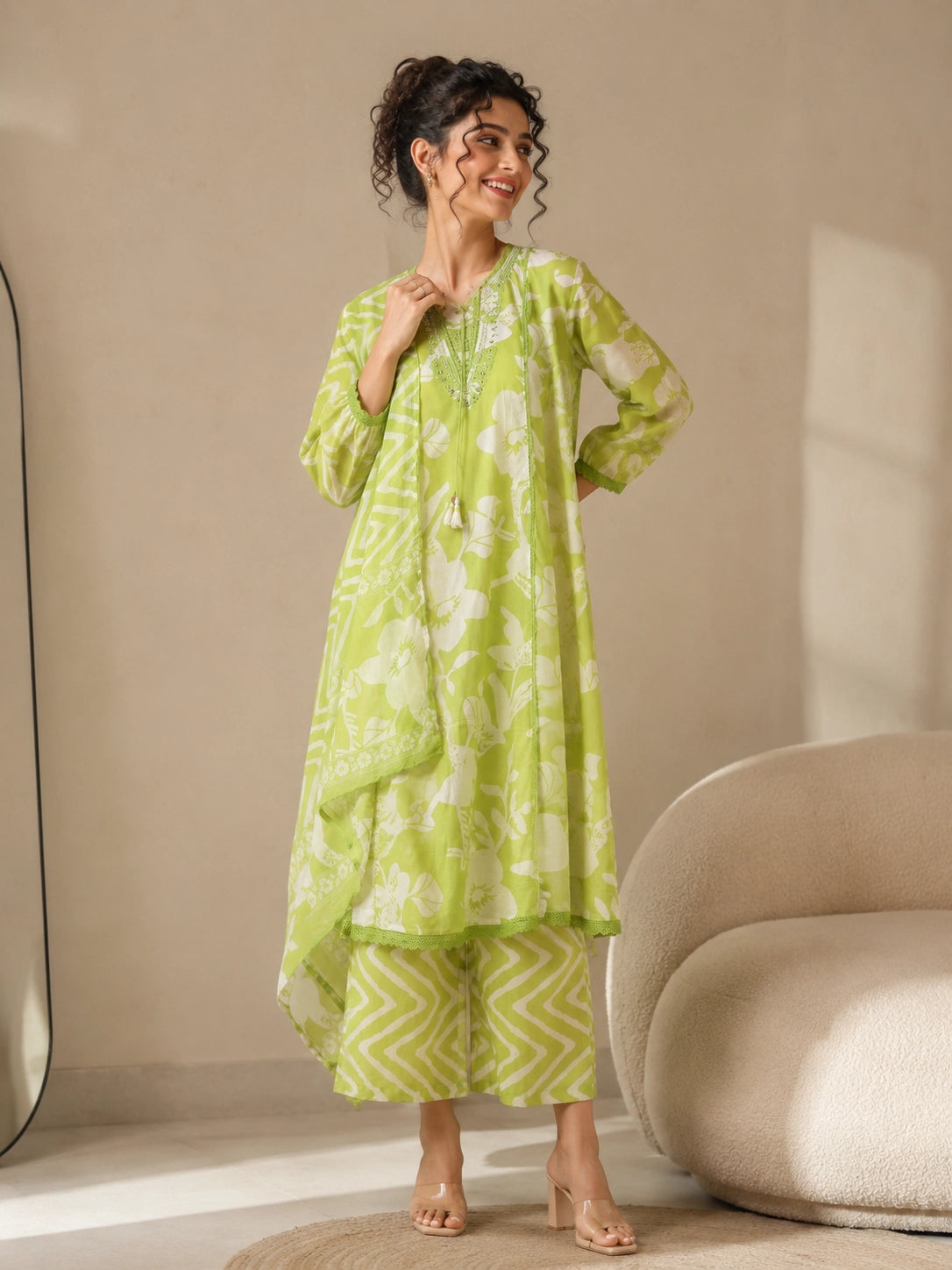 Woman wearing a lime green printed kurti and chevron patterned pants, sitting on a cream sofa.