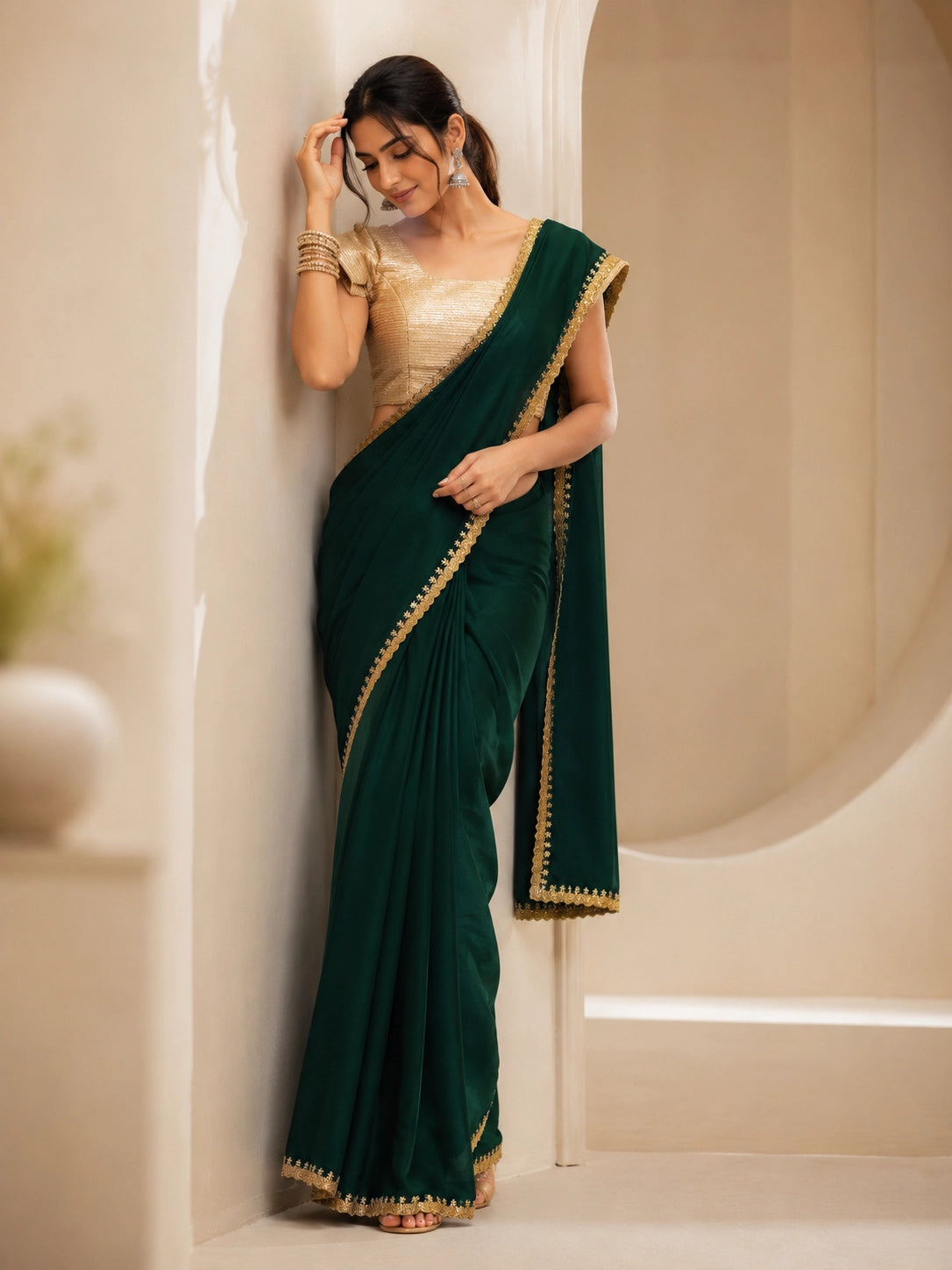 Woman wearing a beautiful emerald green saree with a golden border and matching blouse.