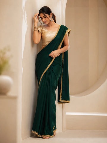 Woman wearing a beautiful emerald green saree with a golden border and matching blouse.