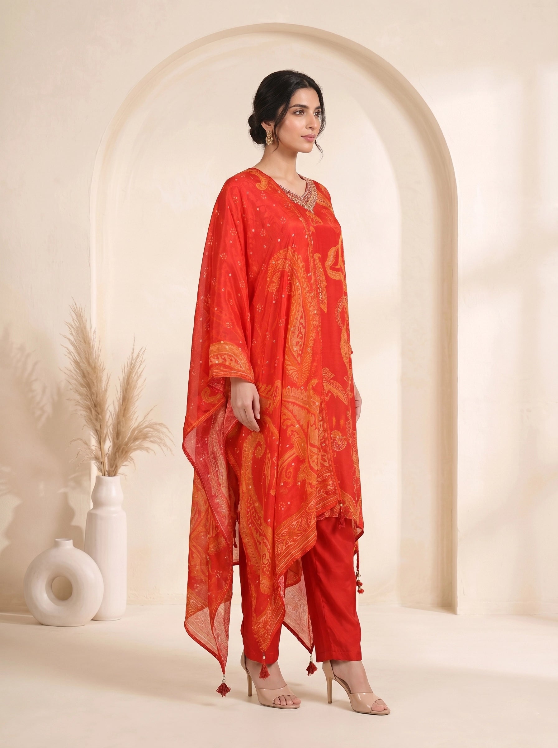 Woman wearing a vibrant orange kurti with paisley print and matching pants, adorned with neckline embellishments.