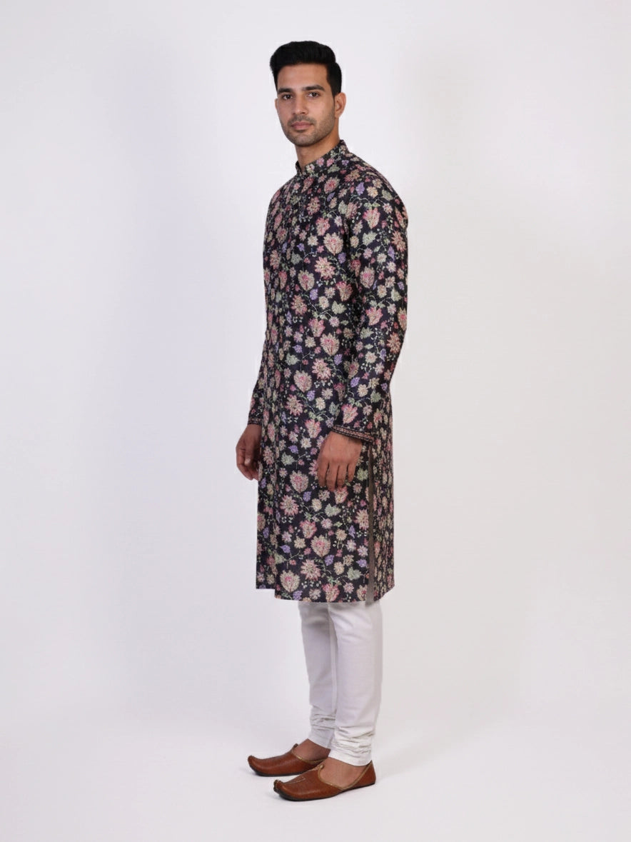 Man wearing a dark multi-color floral print kurta and white churidar pants, traditional ethnic wear.