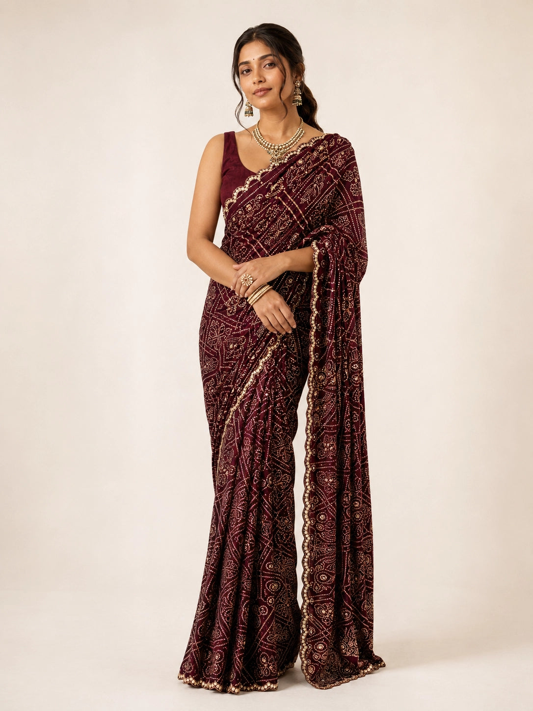 Woman wearing a maroon saree with gold bandhani patterns and a matching sleeveless blouse.