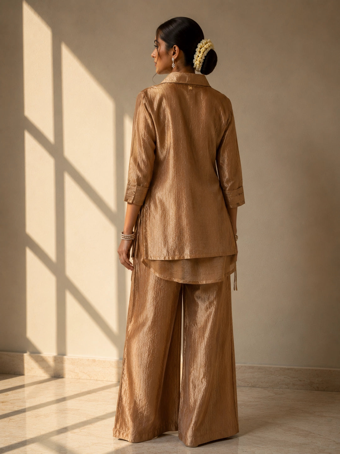 Woman wearing a shimmering brown kurti set with a heavily embroidered gold neckline.