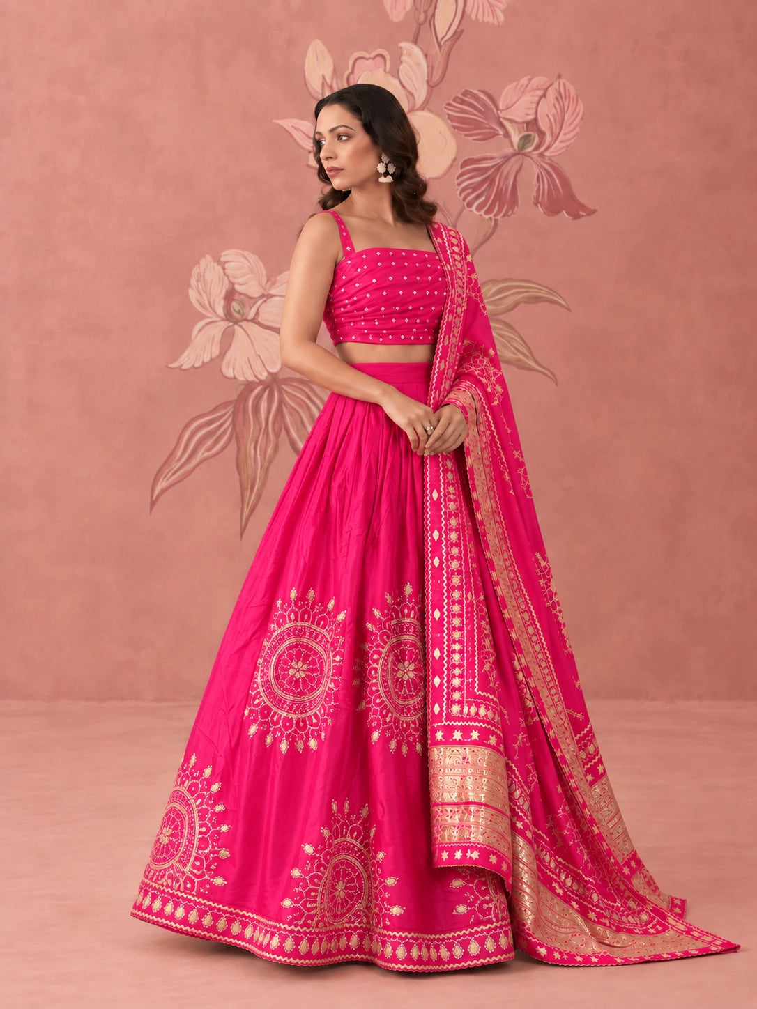 Woman wearing a vibrant rani pink lehenga set with intricate gold embroidery and matching dupatta.