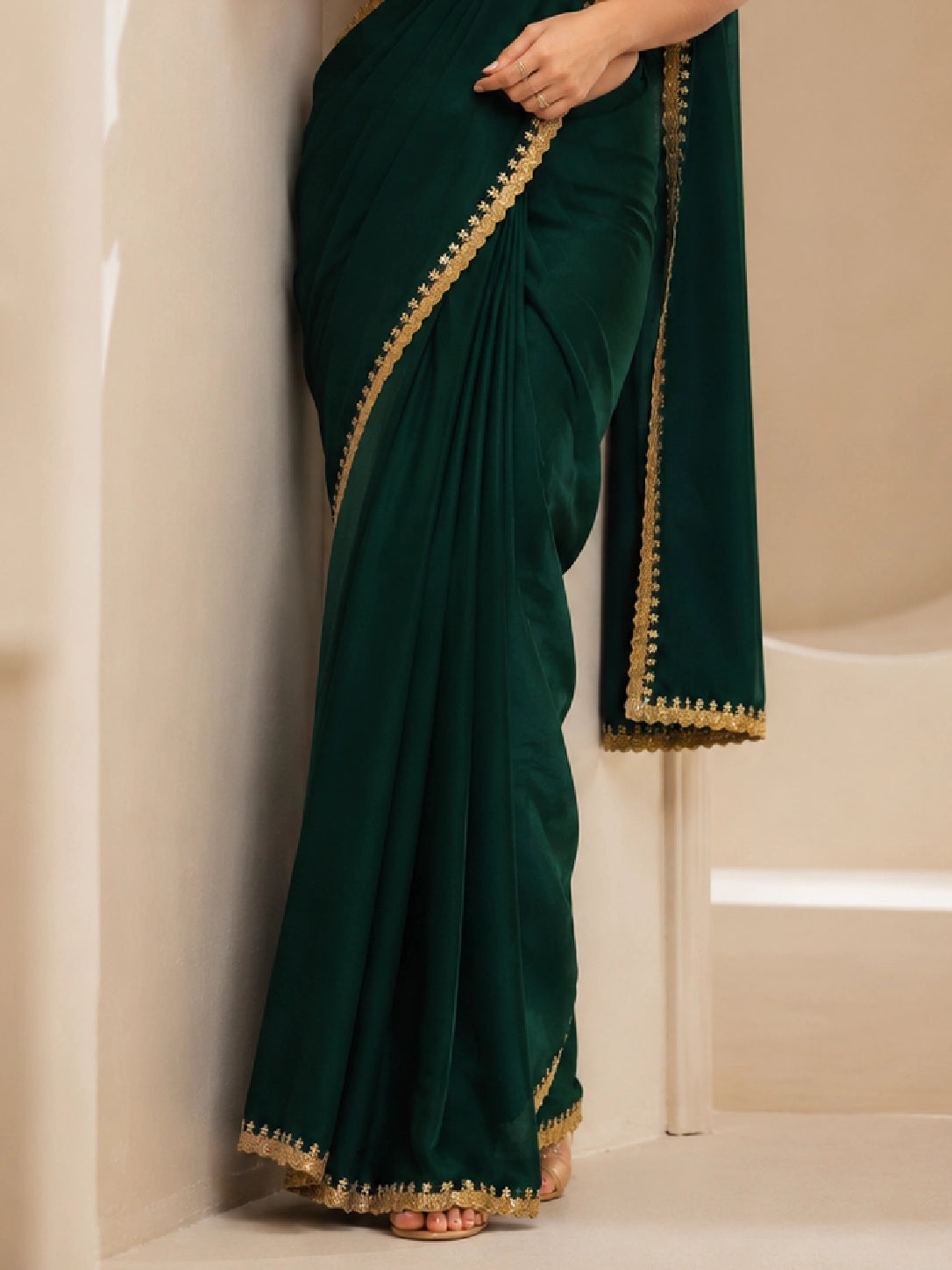 Woman wearing a beautiful emerald green saree with a golden border and matching blouse.