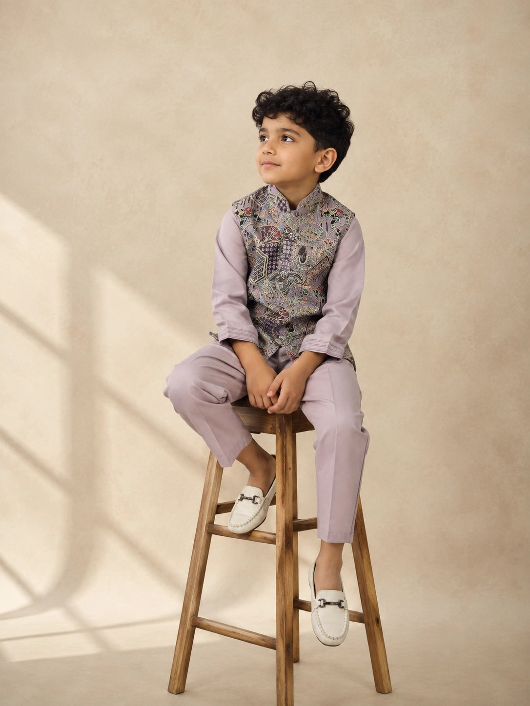 Young boy wearing a levendar kurta pajama with an intricately patterned waistcoat.