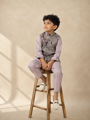 Young boy wearing a levendar kurta pajama with an intricately patterned waistcoat.