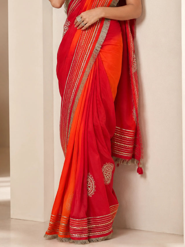 Woman elegantly draped in a vibrant red and orange ombre saree with silver borders.