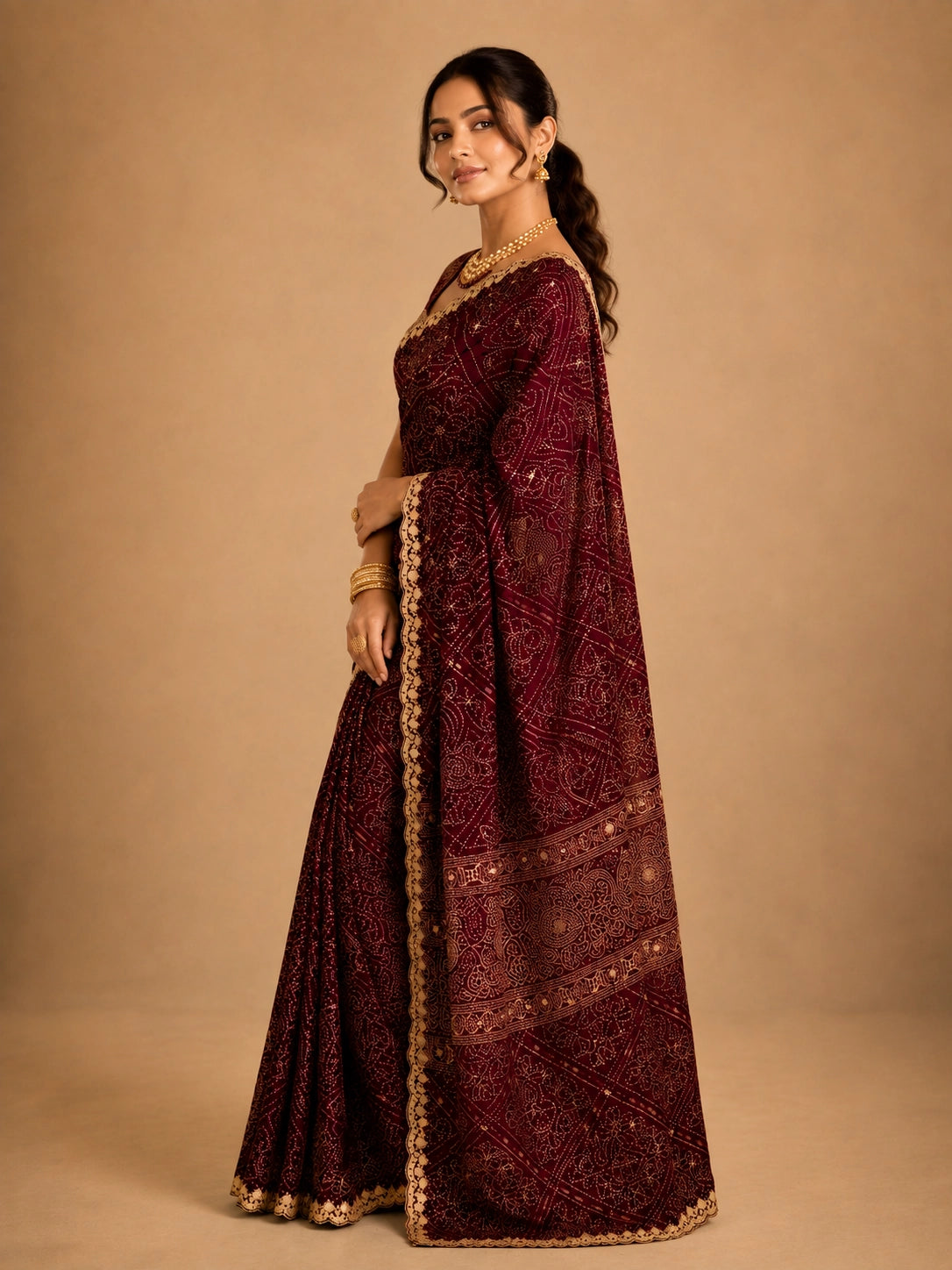 Woman in a maroon bandhani saree with intricate gold embroidery and border.
