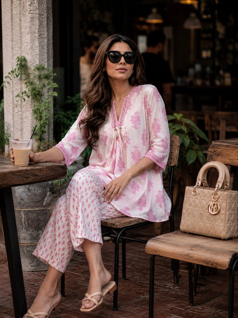 Woman wearing a pink floral print cotton kurta and matching pants, sitting at a table.