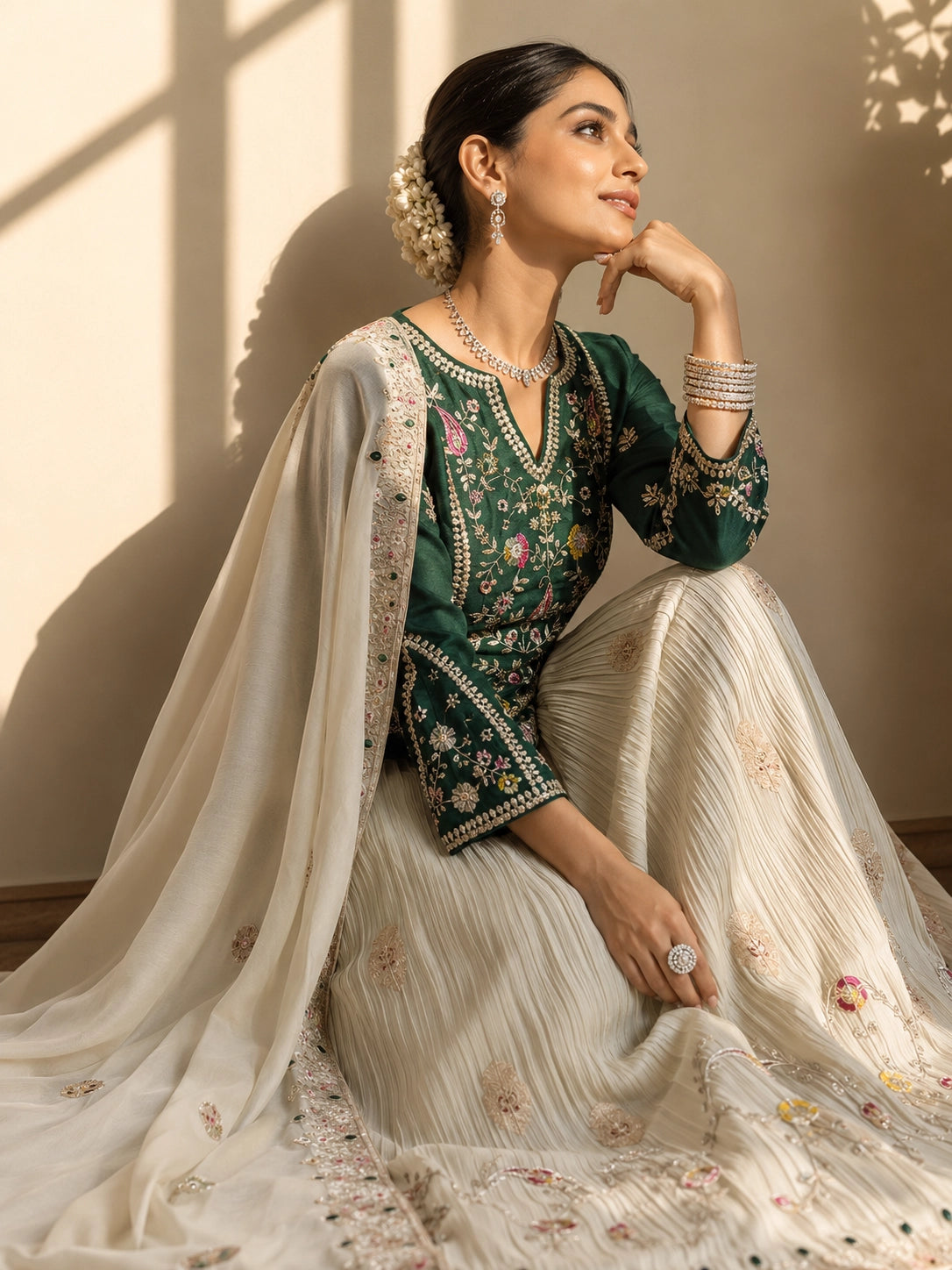 Elegant woman in a dark green embroidered kurta, cream pleated skirt, and matching dupatta.