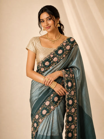 Woman wearing an elegant green embroidered saree with a golden blouse and traditional jewelry.