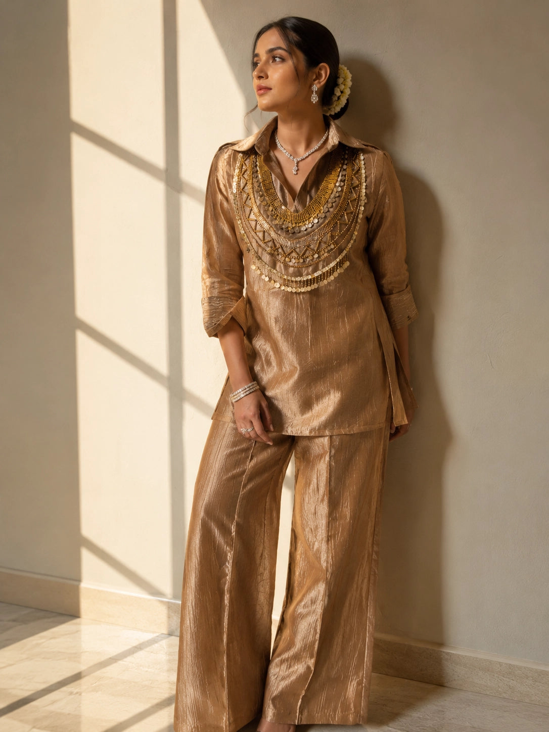 Woman wearing a shimmering brown kurti set with a heavily embroidered gold neckline.