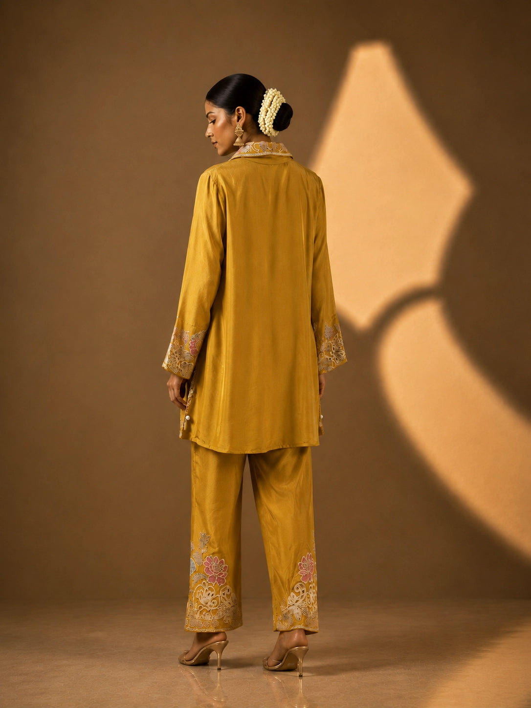 Model in a mustard embroidered kurti set with pastel floral patterns and matching pants.