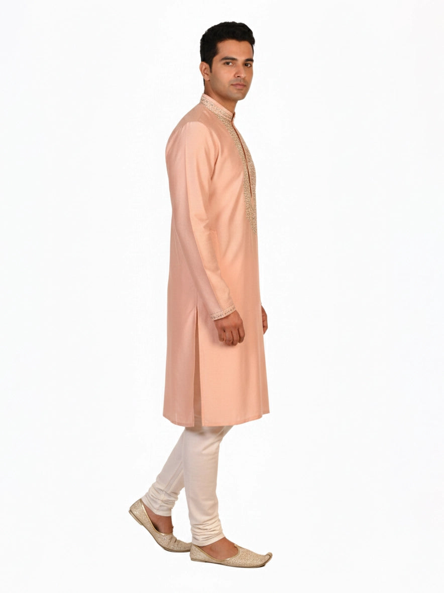 Man wearing a peach silk Kurta Pajama with intricate embroidery on the neckline and cream churidar pants.