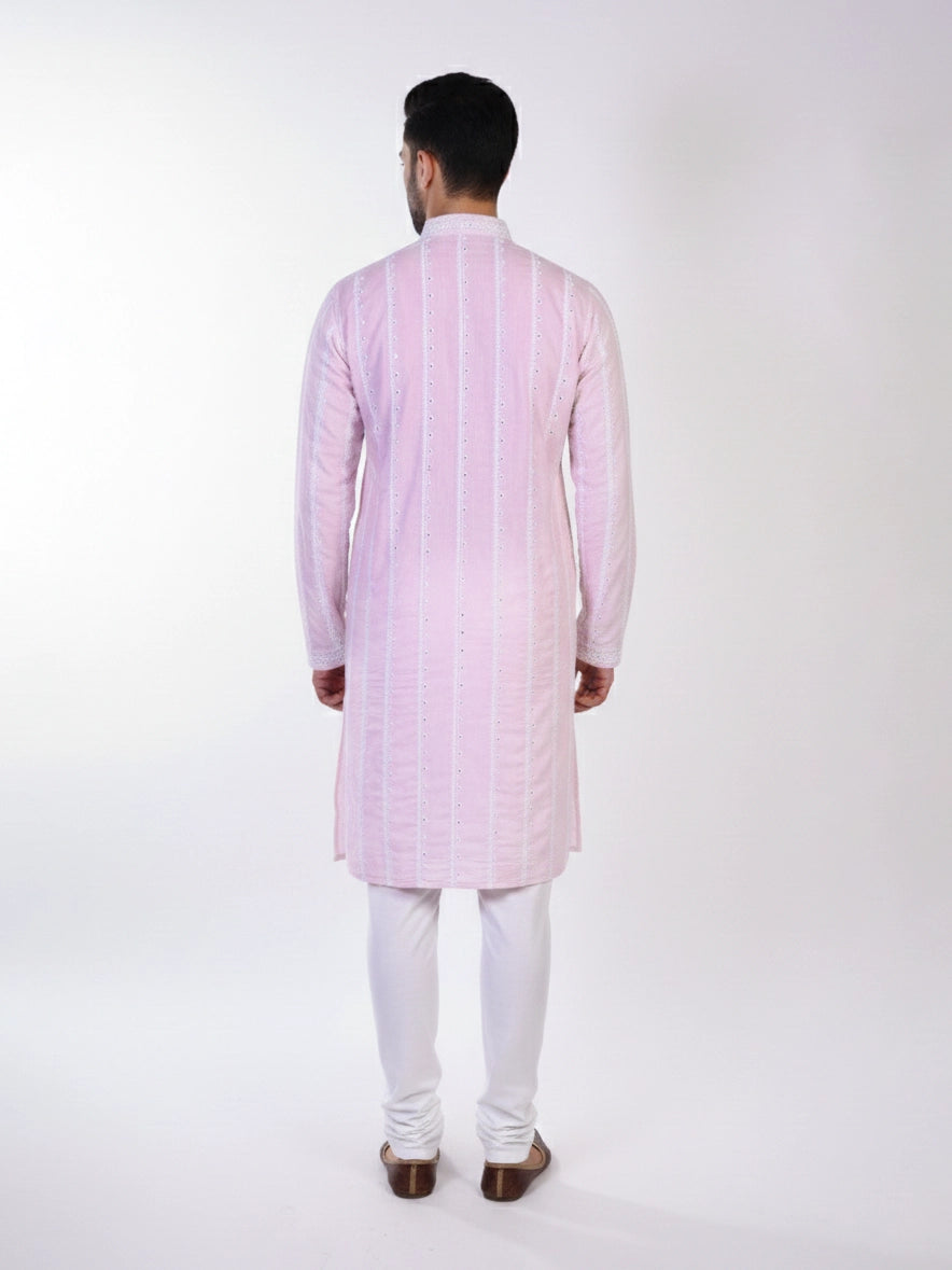 Man wearing a pink chikankari kurta with white churidar pants and brown embellished juttis.