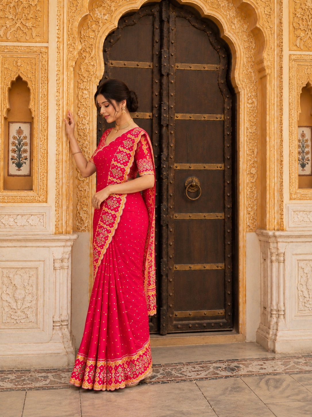 Woman in a vibrant red  saree with golden embroidery sitting on steps.