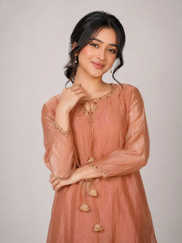 Woman wearing a peach embroidered kurta with gold tassels and a tie-neck detail.