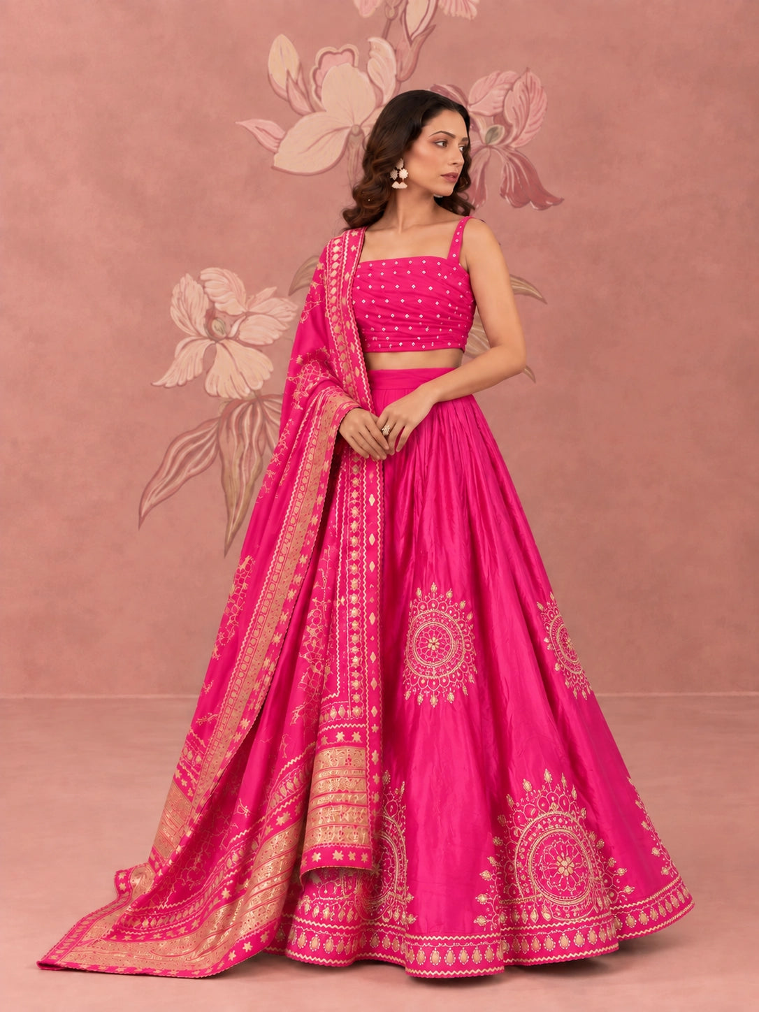 Woman wearing a vibrant rani pink lehenga set with intricate gold embroidery and matching dupatta.