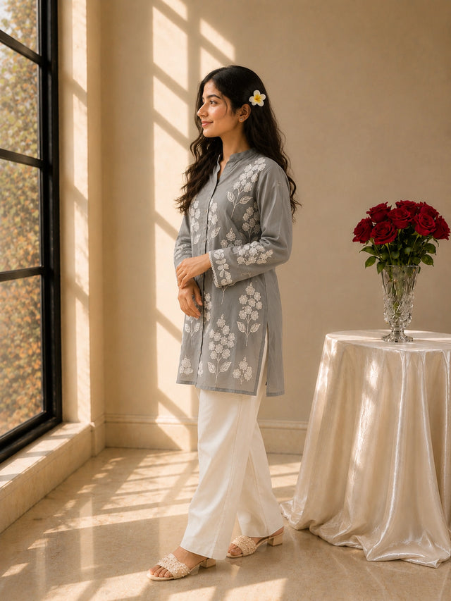 Woman wearing a sky blue embroidered tunic with white pants and sandals.