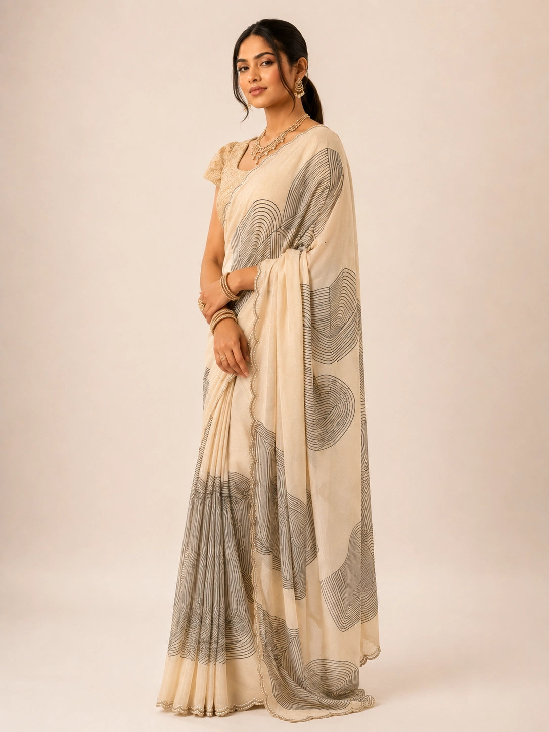 Woman in cream  saree with black abstract print and gold embellished blouse.