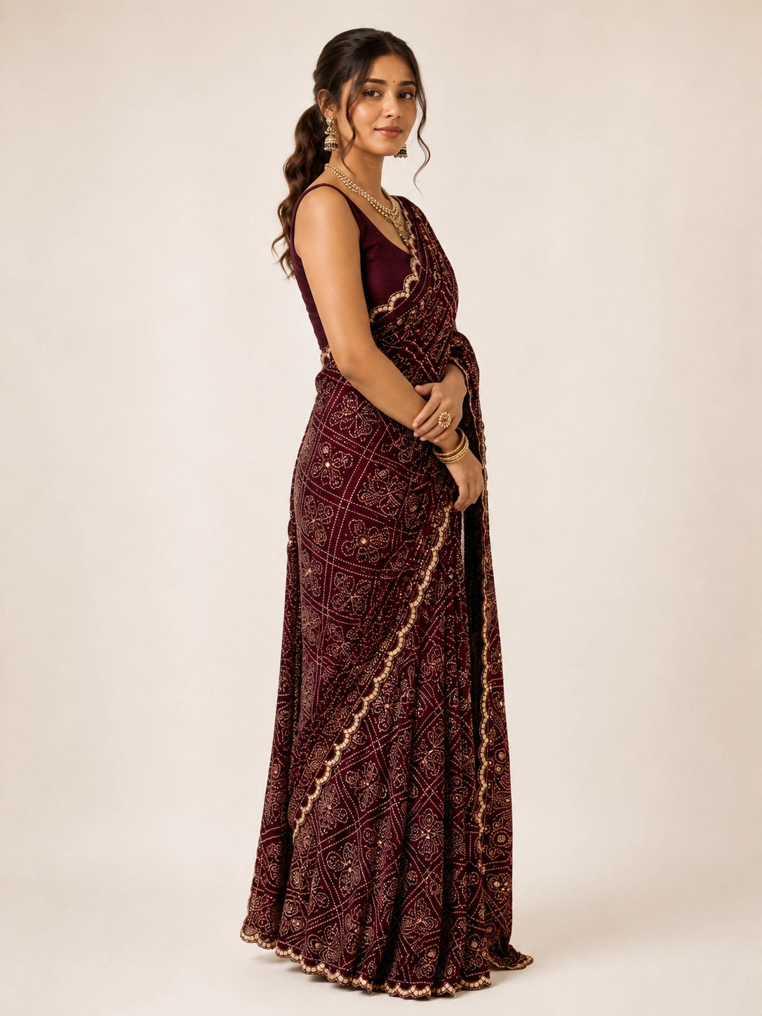 Woman wearing a maroon saree with gold bandhani patterns and a matching sleeveless blouse.