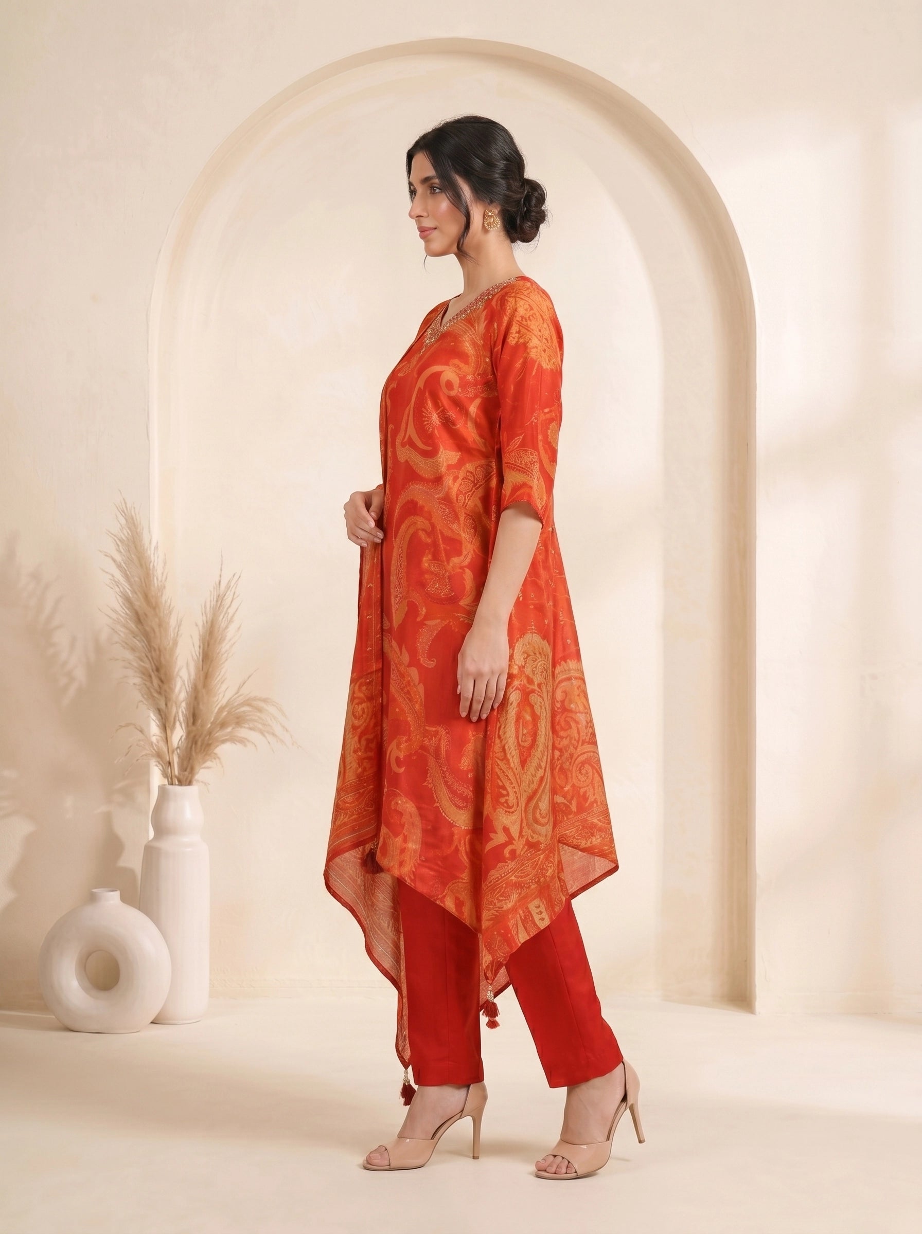 Woman wearing a vibrant orange kurti with paisley print and matching pants, adorned with neckline embellishments.
