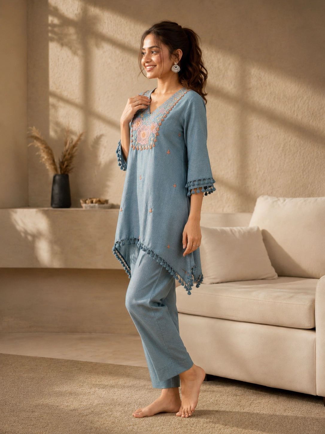 Woman wearing a blue linen co-ord set with floral embroidery and tassel details, sitting and reading a book.