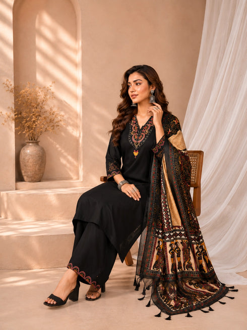 Woman wearing a black embroidered kurti and palazzo set with a colorful printed dupatta, seated on a chair.