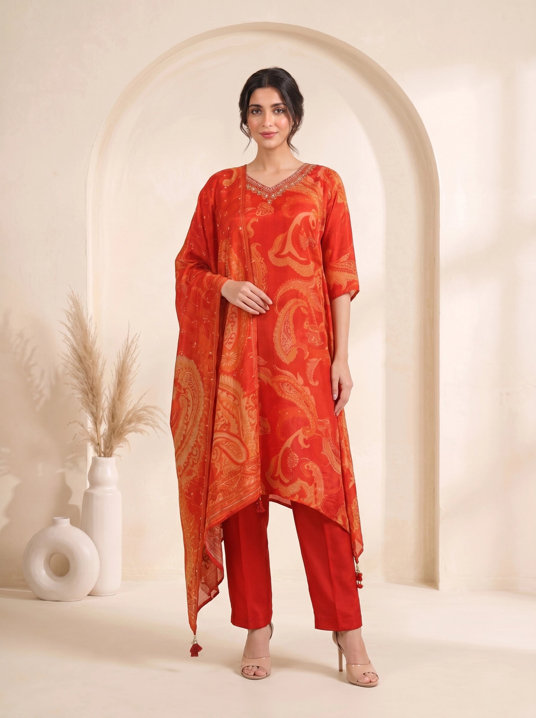 Woman wearing a vibrant orange kurti with paisley print and matching pants, adorned with neckline embellishments.