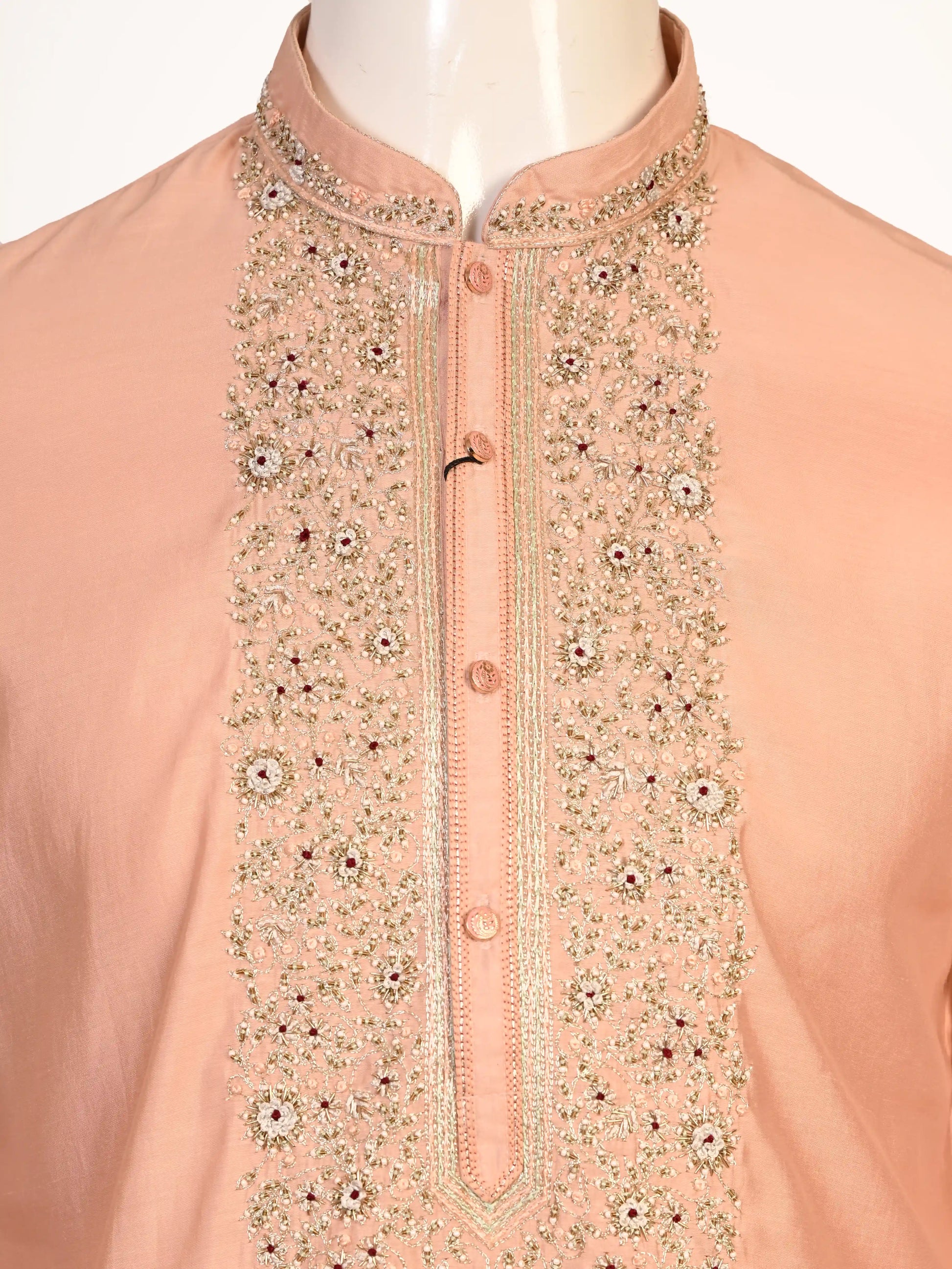 Man wearing a peach silk Kurta Pajama with intricate embroidery on the neckline and cream churidar pants.
