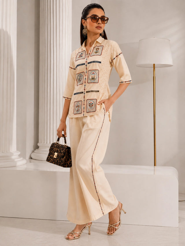 Woman wearing a cream embroidered shirt and wide-leg pants, sitting with a leopard print handbag.