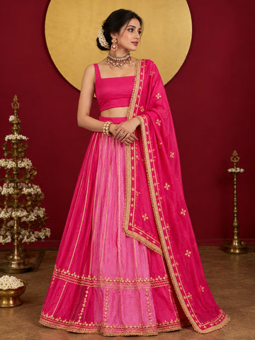 Woman in a vibrant rani pink ombre lehenga choli with gold embroidery.