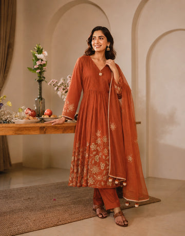 Woman smiling in a rust embroidered Anarkali kurti set with matching dupatta.