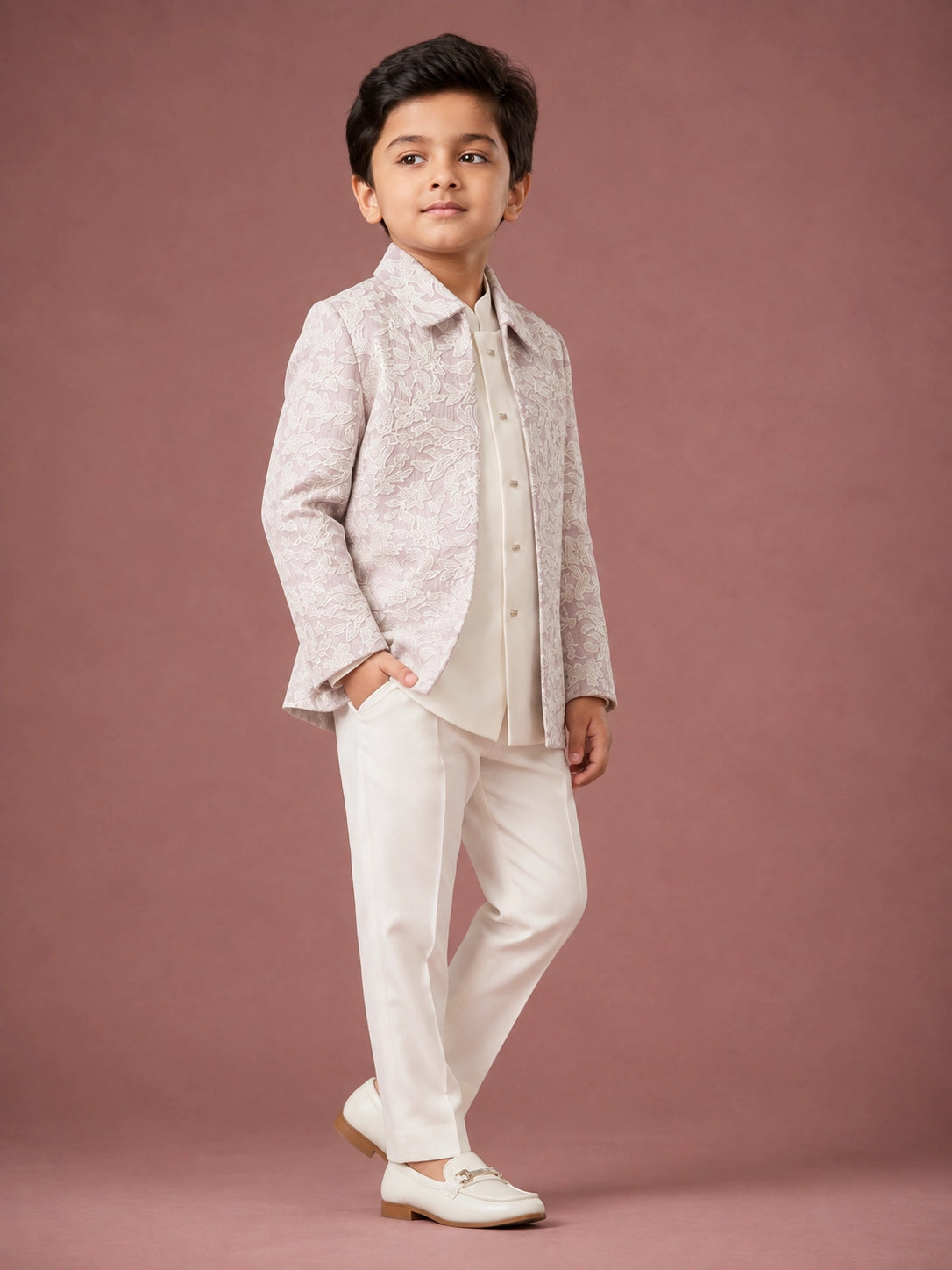Young boy in a light pink patterned IndoWestern jacket, white kurta, and white trousers.