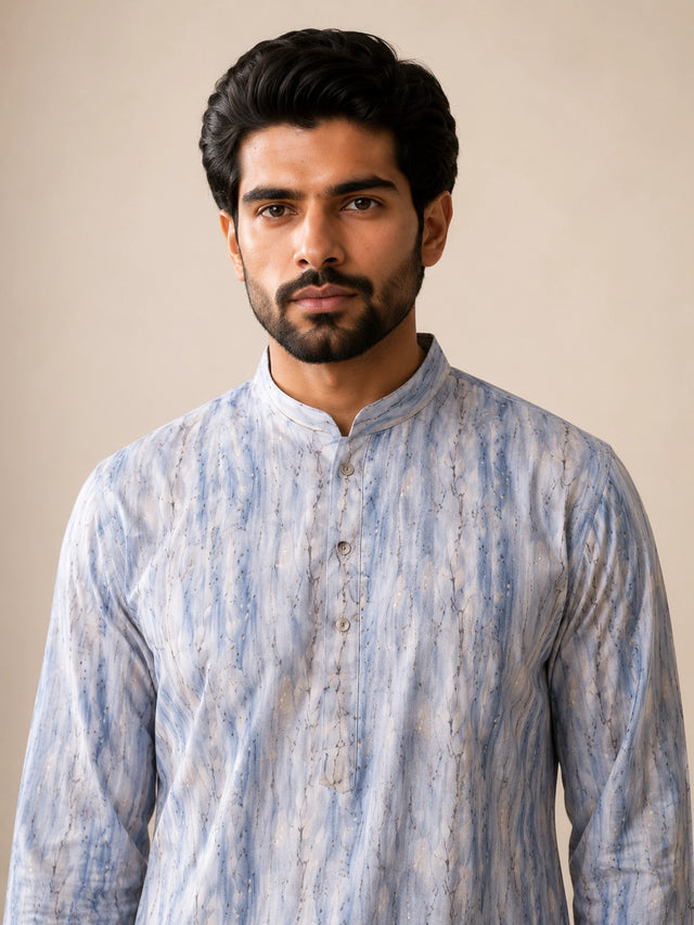 Man in a dust blue printed kurta, white pajama, and brown loafers.