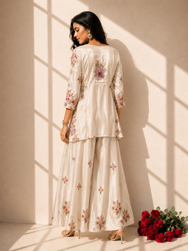 Woman in elegant cream floral embroidered kurti set with sharara and dupatta.