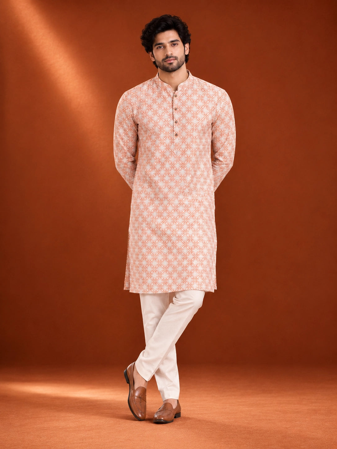 Man wearing an orange and white geometric printed kurta with white pajama and brown loafers.