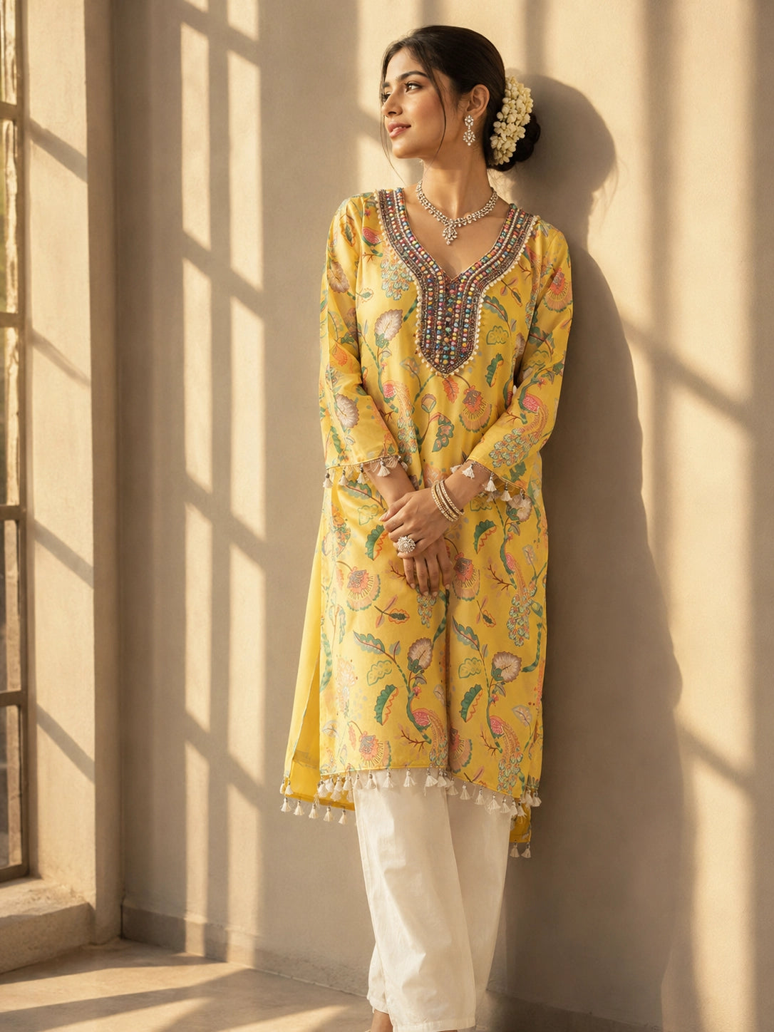 Woman wearing a vibrant yellow floral kurti with intricate embroidered V-neck and tassels.