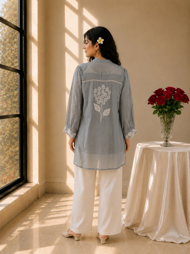 Woman wearing a sky blue embroidered tunic with white pants and sandals.