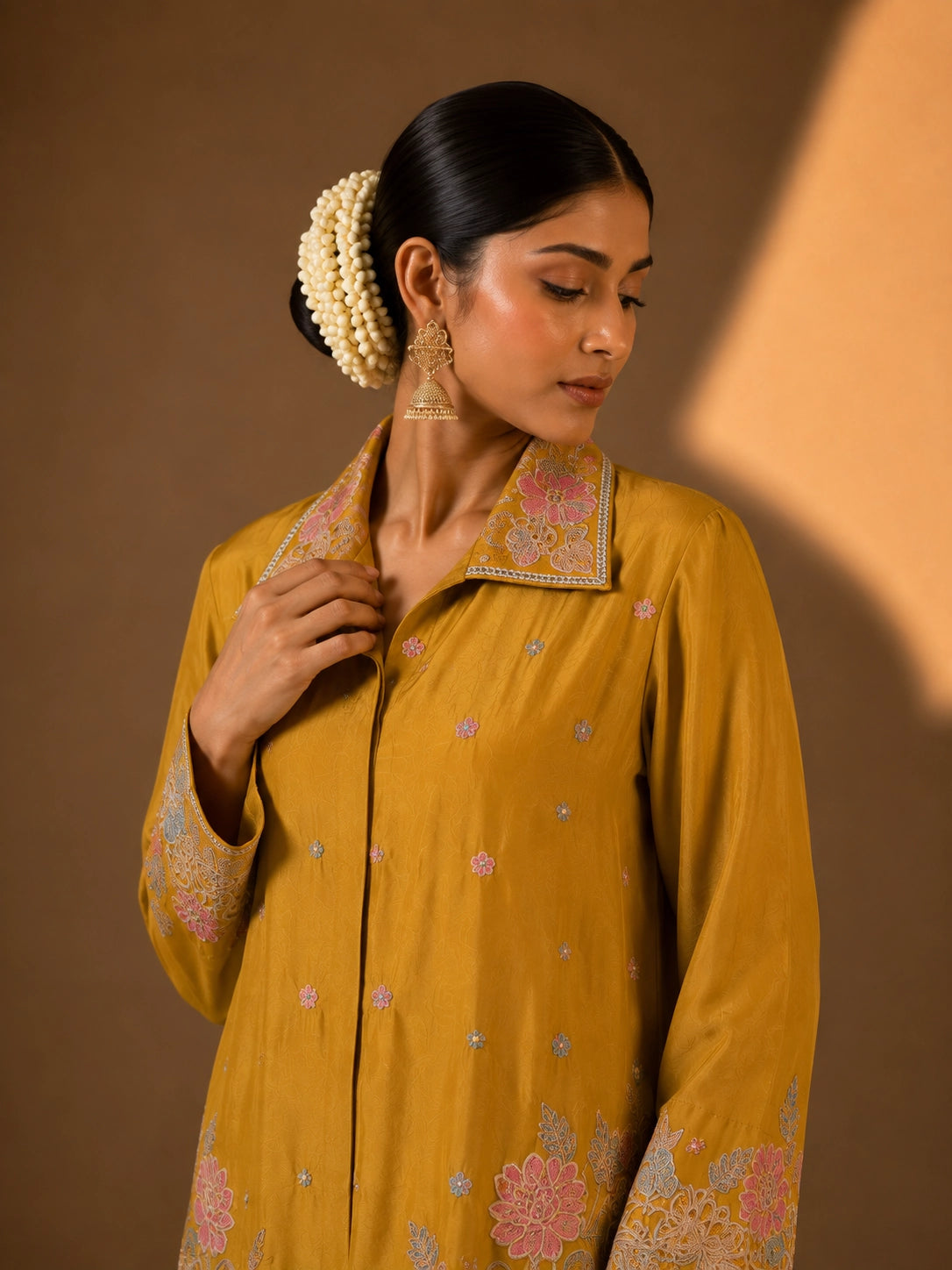 Model in a mustard embroidered kurti set with pastel floral patterns and matching pants.