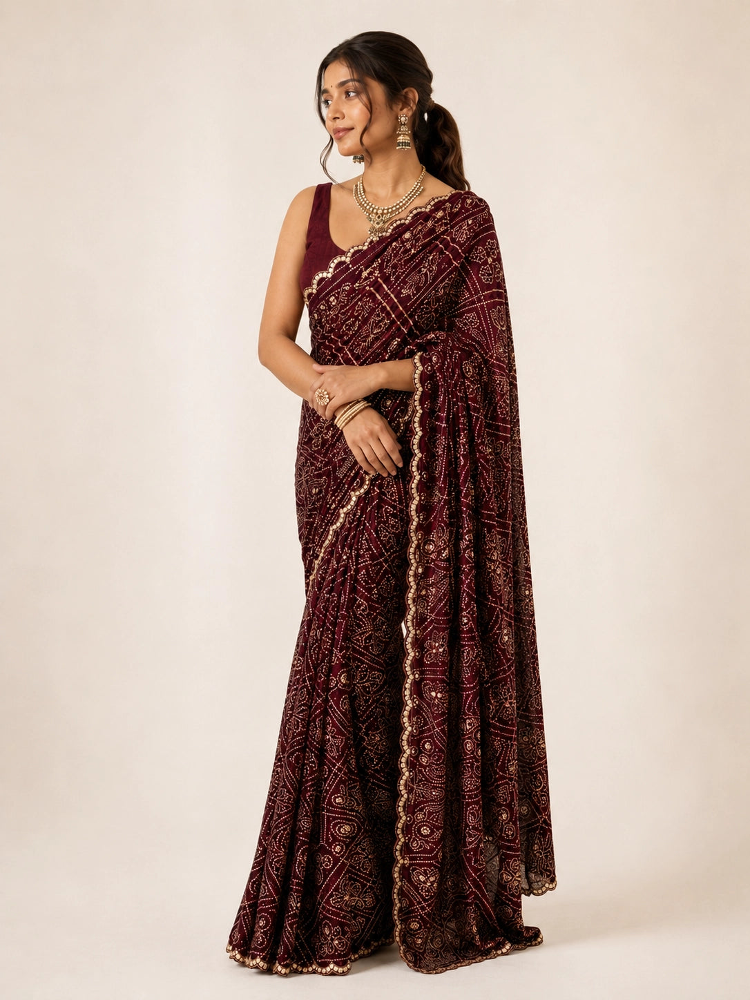 Woman wearing a maroon saree with gold bandhani patterns and a matching sleeveless blouse.