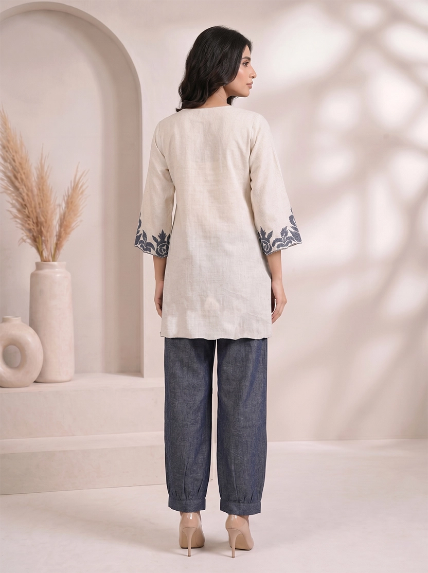 Woman wearing a beige embroidered V-neck kurta with dark blue palazzo pants, styled for a casual occasion.