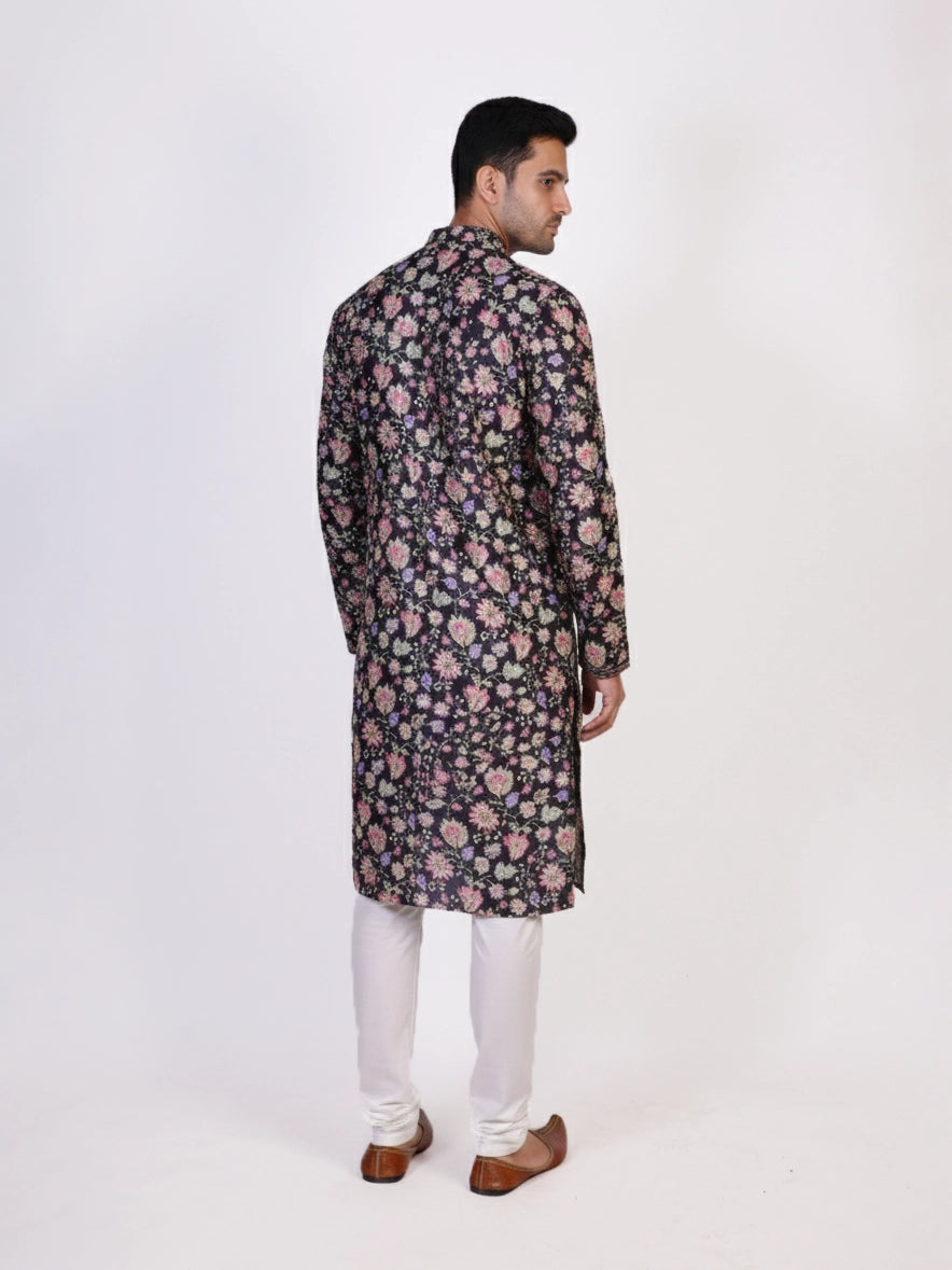 Man wearing a dark multi-color floral print kurta and white churidar pants, traditional ethnic wear.