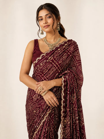 Woman wearing a maroon saree with gold bandhani patterns and a matching sleeveless blouse.
