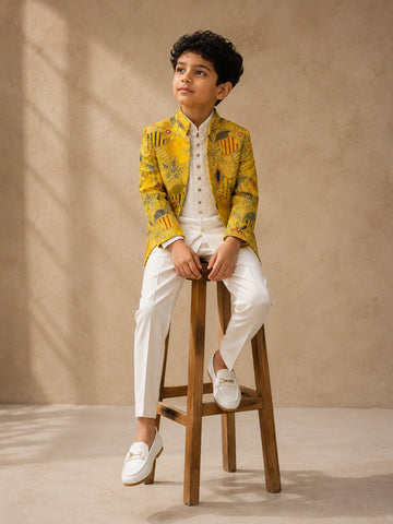 Young boy wearing a mustard patterned bandhgala jacket, off-white kurta, and white trousers.