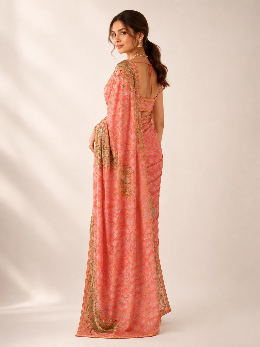 Woman in an elegant peach saree with intricate gold embroidery and matching blouse.